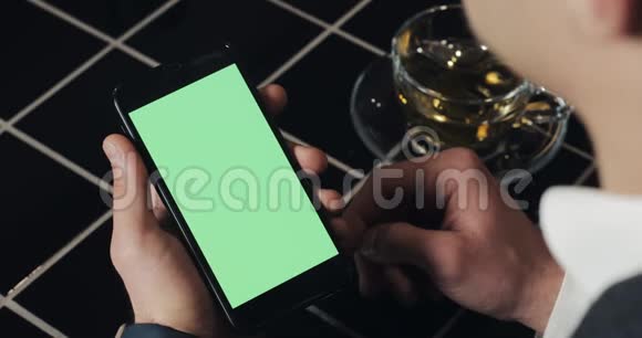 年轻的商人使用带有绿色屏幕触摸板的smarthpone并在咖啡馆打手势接近一个拿着手机的家伙敲视频的预览图