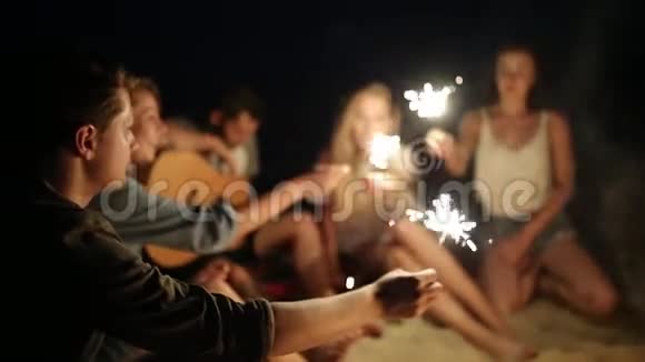 在日落黄昏时朋友们在海滩上闪闪发光地庆祝年轻男女围坐在篝火旁视频的预览图