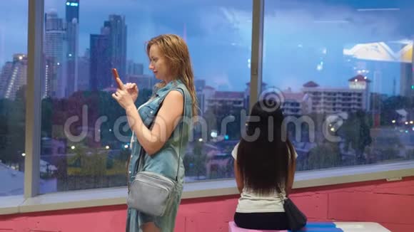 站在摩天大楼背景下窗前的湿漉漉的金发女孩在外面下雨的时候用手机视频的预览图