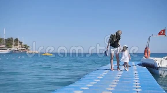 母亲和女孩走在码头上波浪摆动视频的预览图