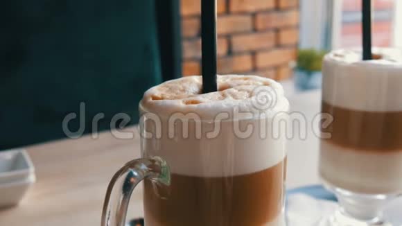 咖啡拿铁牛奶和空气泡沫黑色吸管站在透明的特殊玻璃桌上时髦的咖啡馆视频的预览图