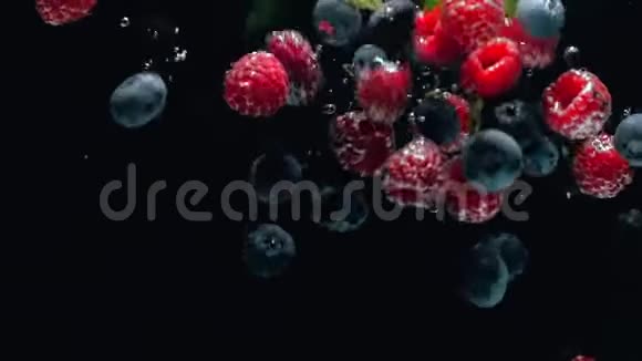 带着蓝莓和薄荷叶的新鲜覆盆子落在水中的黑色背景上溅在黑色的背景上视频的预览图