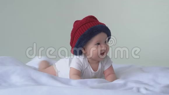 快乐的宝贝女儿戴帽子的孩子躺在床上笑白色背景视频的预览图
