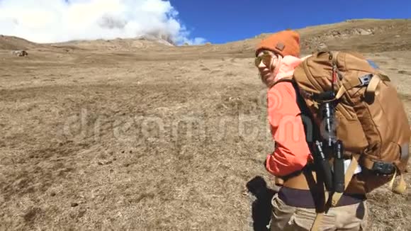快乐的旅行女孩摄影师带着相机和背包在白雪皑皑的背景下上山视频的预览图
