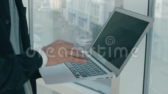 无法辨认的人在现代办公室全景窗口附近的笔记本电脑上工作背景上的城市景观视频的预览图