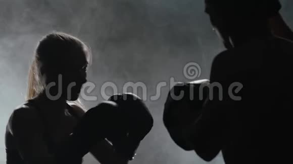 戴着女拳击手套的人在黑暗中在擂台上打剪影烟雾背景慢动作视频的预览图