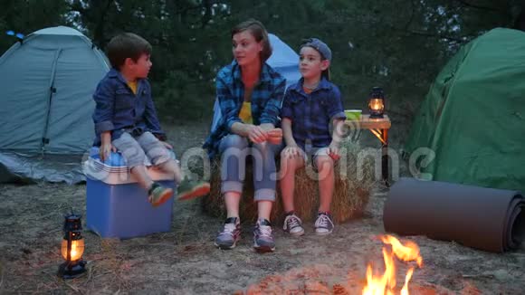 一家人在户外度假妈妈和两个孩子坐在篝火旁的草包里妈妈和孩子们视频的预览图