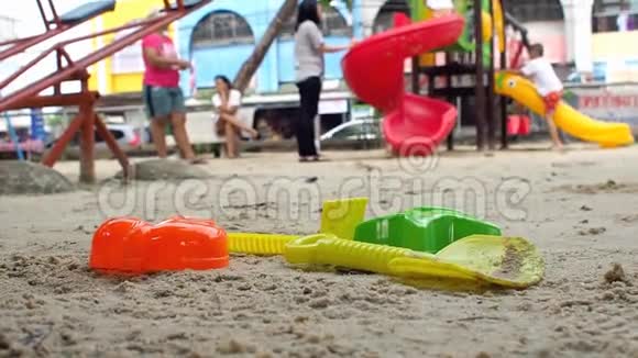 玩具挖沙它有一个美丽的颜色躺在沙子上背景是一个操场有孩子和成年人视频的预览图