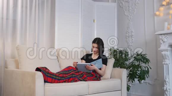 漂亮的年轻女人躺在沙发上看书视频的预览图