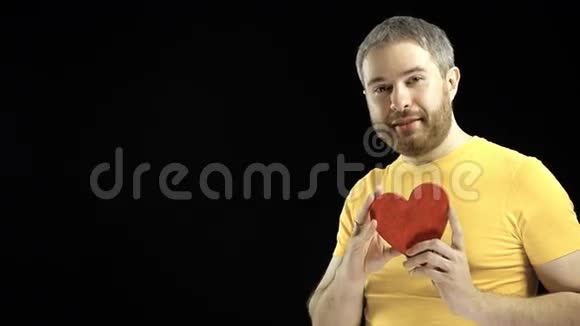 穿黄色T恤的英俊男子抱着红色的心形爱情浪漫约会关系概念黑色背景4K视频的预览图