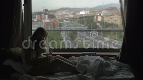 西班牙巴塞罗那母亲躺在床上小儿子靠着巨大的全景窗户和城市景观视频的预览图