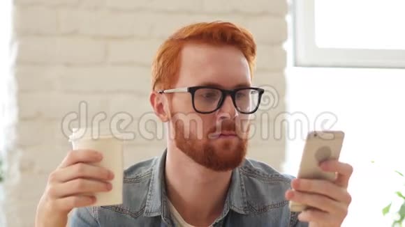使用智能手机电话饮用咖啡茶的胡子和红发男士视频的预览图