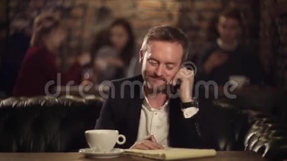 一个漂亮的成功男人在办公室打电话在咖啡馆里写笔记本视频的预览图