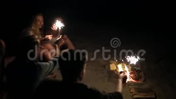 在日落黄昏时朋友们在海滩上闪闪发光地庆祝年轻男女围坐在篝火旁视频的预览图