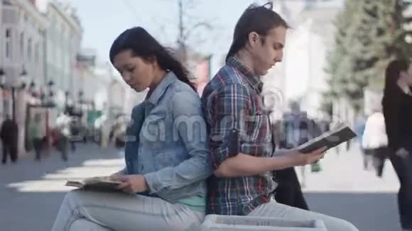可爱的女孩和留着长发的男孩在街上看书视频的预览图