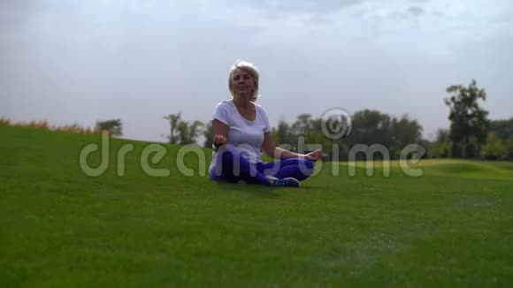 成熟的女人坐在公园的草地上视频的预览图