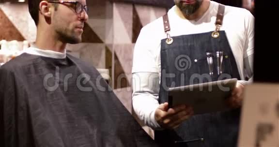 男理发师向顾客展示数码平板电脑视频的预览图