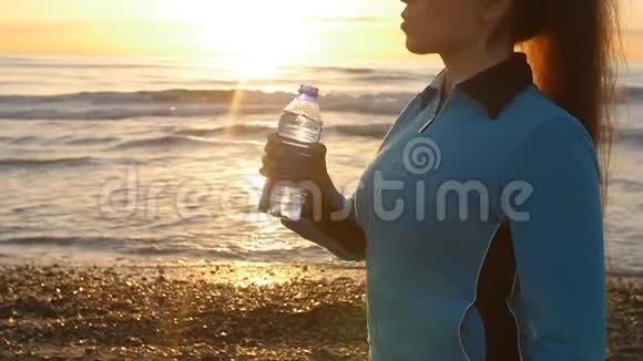 在海边日落时喝水的女人视频的预览图