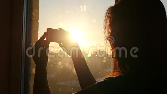 日落时分年轻漂亮的女孩在靠近窗户的地方开着手机动作慢高清视频的预览图