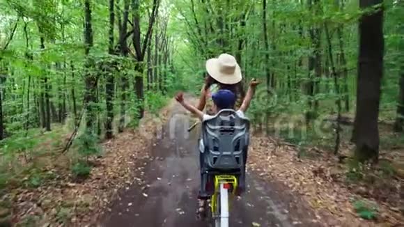 一个戴着帽子和衣服的女人带着一篮子花和一个小孩子一起骑自行车在森林里在森林里在森林里视频的预览图