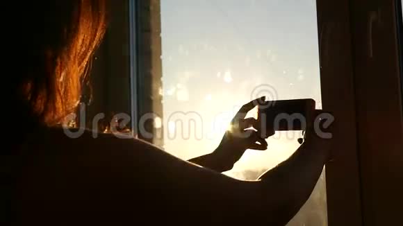 日落时分美丽的女孩在窗外拍照高清视频的预览图
