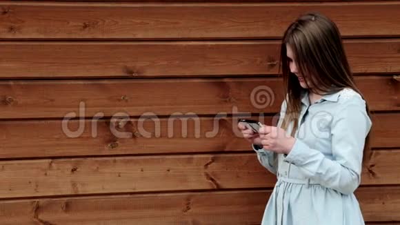 年轻女孩拿着她的智能手机在可爱的姿势木制背景复制空间视频的预览图