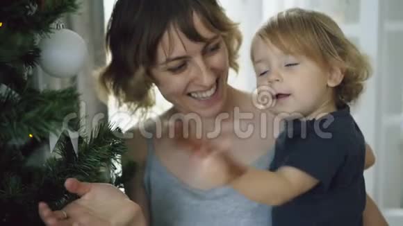 快乐的母亲和她的小女儿在家中的圣诞树旁玩耍视频的预览图