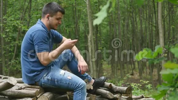 一个年轻的帅哥在树林里听耳机里的音乐视频的预览图