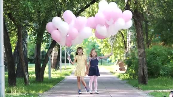 两个小女孩手里拿着气球的肖像夏日公园快乐无忧无虑的孩子们视频的预览图
