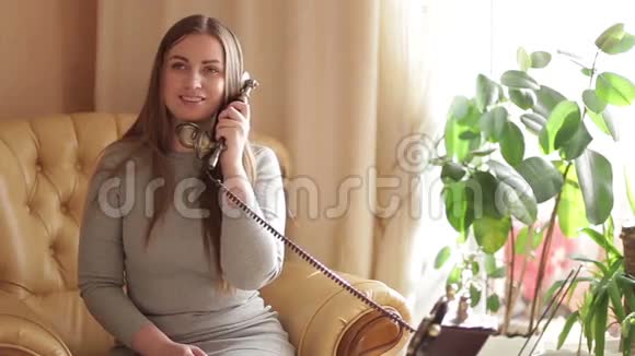 年轻的女人坐在沙发上打电话背景中绿花出焦美丽美丽视频的预览图