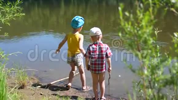两个孩子在河岸上用钓鱼竿钓鱼美丽的夏日风景户外娱乐活动视频的预览图