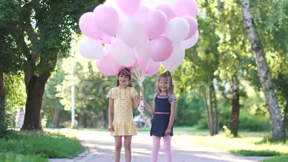 两个小女孩手里拿着气球的肖像夏日公园里快乐无忧无虑的孩子们视频的预览图
