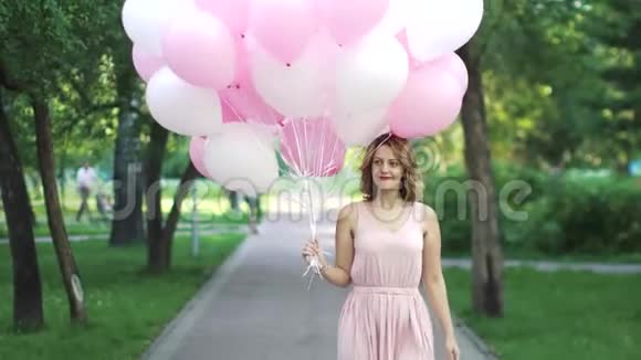 美丽的年轻女子高兴地在一个夏天的公园里拿着气球视频的预览图