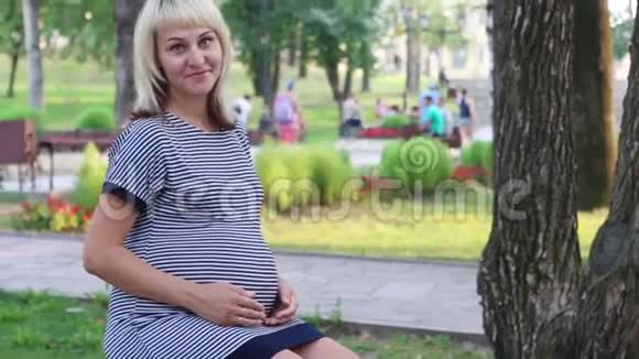 孕妇坐在长凳上微笑着抚摸她的腹部视频的预览图