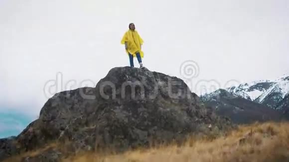 一个穿着黄色斗篷的年轻女孩沿着岩石跑一个旅行者正在山间旅行视频的预览图