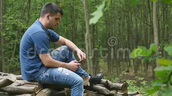 一个年轻的帅哥在树林里听耳机里的音乐视频的预览图