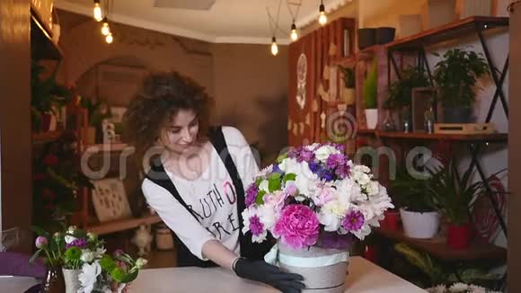 年轻女子在花店当花店花店工看着相机书桌上放着花束微笑视频的预览图