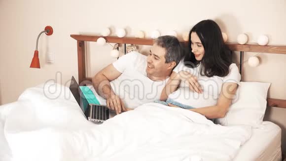 丈夫和怀孕的妻子在床上使用笔记本电脑网上购物视频的预览图