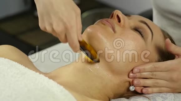 美丽的女人在水疗中心做面部按摩美容院面部皮肤护理慢动作视频的预览图