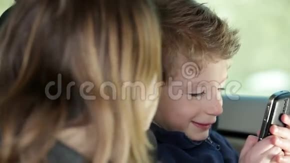 家庭旅行时小男孩在车后座玩手机视频的预览图