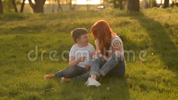 母亲和儿子坐在草地上玩得很开心视频的预览图