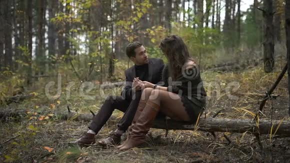 在森林里约会的幸福夫妻微笑的男人和女人坐在树间的原木上视频的预览图