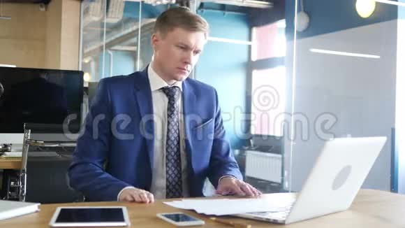 商人开始他的工作日坐在办公桌旁拿着笔记本电脑视频的预览图