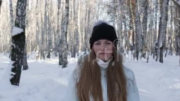 特写镜头中一个美丽的女孩在移动中微笑看着冬林里的相机冬季离焦背景视频的预览图
