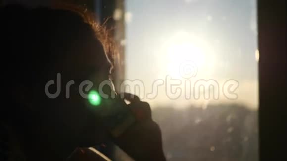 美丽的年轻女孩在背景夕阳下的窗户里说话4K视频的预览图