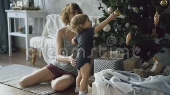 快乐的母亲和她的小女儿在家中的圣诞树旁玩耍视频的预览图