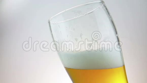 将新鲜啤酒和泡沫倒入装有冰冰冰滴的品脱杯中在白色背景下缓慢运动视频的预览图