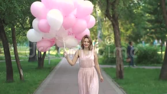 美丽的年轻女子高兴地在一个夏天的公园里拿着气球慢动作视频的预览图