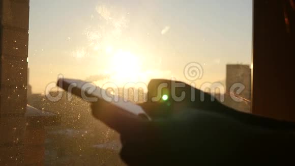 在夕阳的背景下用手握住手机伴随着来自太阳的眩光慢镜头视频的预览图