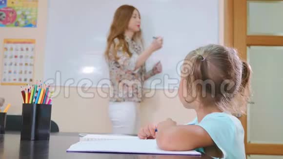 小可爱的女孩坐在教室里和老师一起在练习本上学习视频的预览图